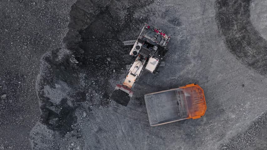 Excavator loading gold and copper ore into dump truck in open pit mine at sunset, mining industry Aerial top view.