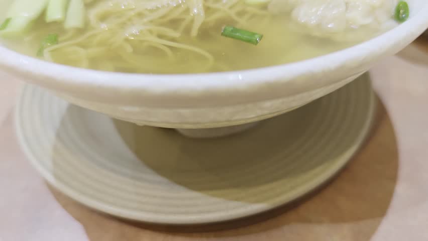 Bowl of freshly cooked steaming hot Wontons (Dumplings) and Egg Noodle Soup. Green vegetables as garnish. Classic Cantonese meal. Catering concept. 4k60.
