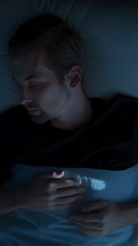 A young man wakes up abruptly in panic, insomnia and a sleep disorder disturb his rest, leaving him fearful, disoriented, and mentally exhausted. Sleep paralysis. Top view. vertical video