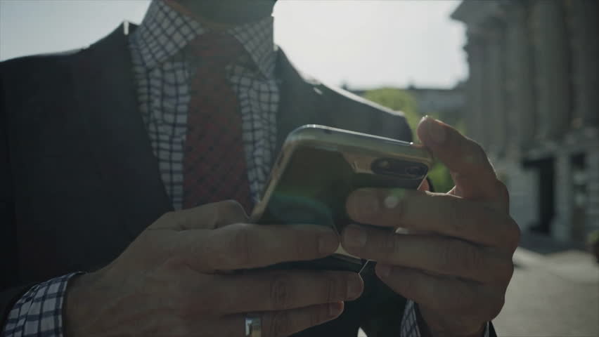 A sophisticated individual with a sleek smartphone stands outside a grand historic building exuding charm