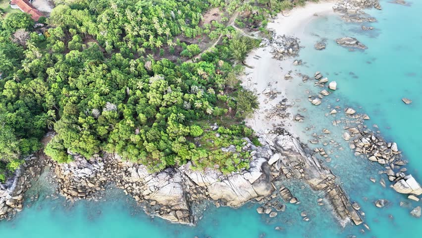 A stunning aerial view of a tropical coastline featuring turquoise waters, granite rock formations, lush green forest, and a pristine white sandy beach in an exotic island paradise.