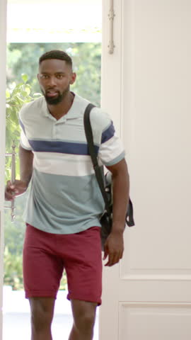 Vertical video: African American father carrying duffel bag and hugging daughter entering foyer. Family, affection, homecoming, bonding, emotional, outdoor view, vertical video