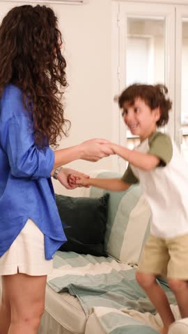 Joyful mother and son share playful moments, jumping and dancing on a comfortable sofa in their living room