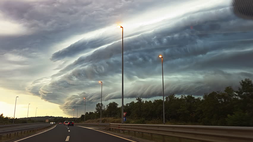 Dramatic storm clouds over highway at sunset. Massive shelf cloud formation looms over a quiet highway at dusk, signaling an approaching storm and turbulent weather.