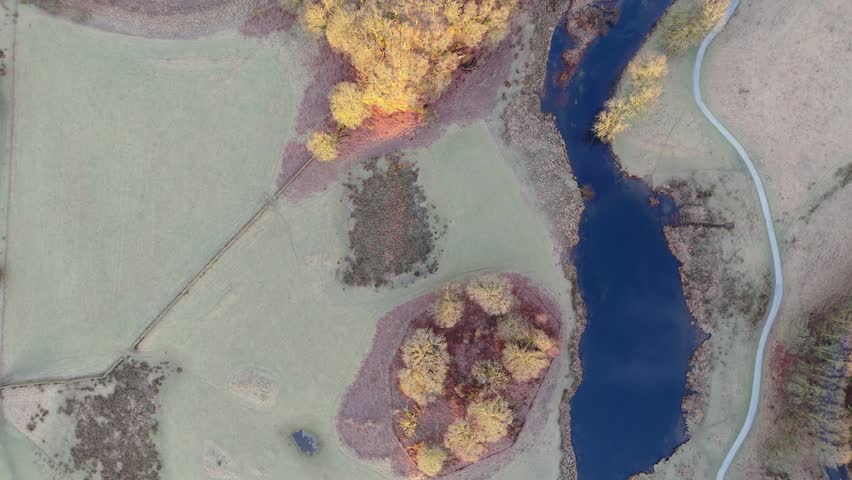 Overhead perspective of a river and pathway in a vibrant landscape. An aerial view showcases a serene landscape featuring a river, trees, and a winding path, offering a peaceful, nature-filled scene.