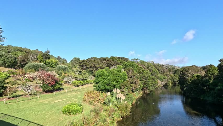 A beautiful and serene landscape view of a river with lush green banks and rolling hills in the New Zealand countryside