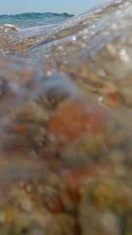 Vertical video, Close-up from the bottom level, Surf zone on a pebble beach, wave after wave covers the camera, Underwater view, slow motion