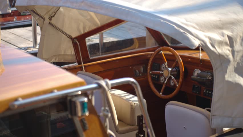 Close up of wooden steering wheel and dashboard inside motorboat cabin. Motor boat bobbing on sea waves. Concept of boating, water transport and luxury travel