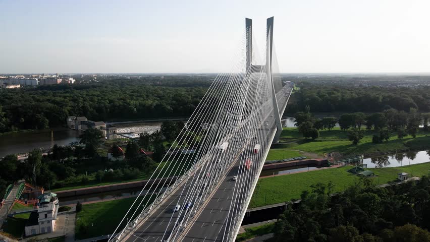 Aerial view of modern cable-stayed bridge over river with traffic and surrounding fields. Car driving on Redzinski bridge in Wroclaw, Poland. Concept of transportation and urban infrastructure