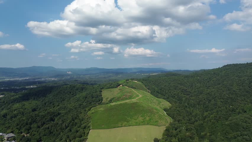 4K aerial video of Wakakusa Hill in Nara, Japan, featuring lush green hills, winding trails, and a vast landscape with forests, mountains, and a bright blue sky.