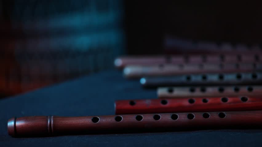 A cinematic rack focus reveals a set of traditional wooden flutes,  resting in a dark room with moody red and blue atmospheric lighting.