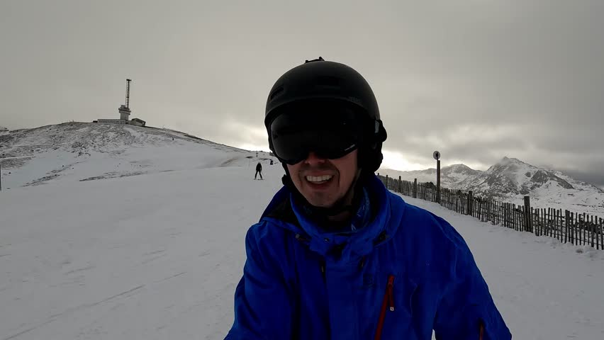 Happy skier wearing blue jacket and helmet smiles at camera while skiing down snowy mountain slope