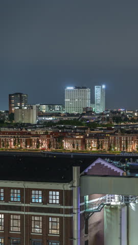 Panoramic aerial timelapse of Katendrecht peninsula and Maashaven harbour at night in Rotterdam, The Netherlands. City skyline, illuminated modern skyscrapers and former factory with waterfront houses