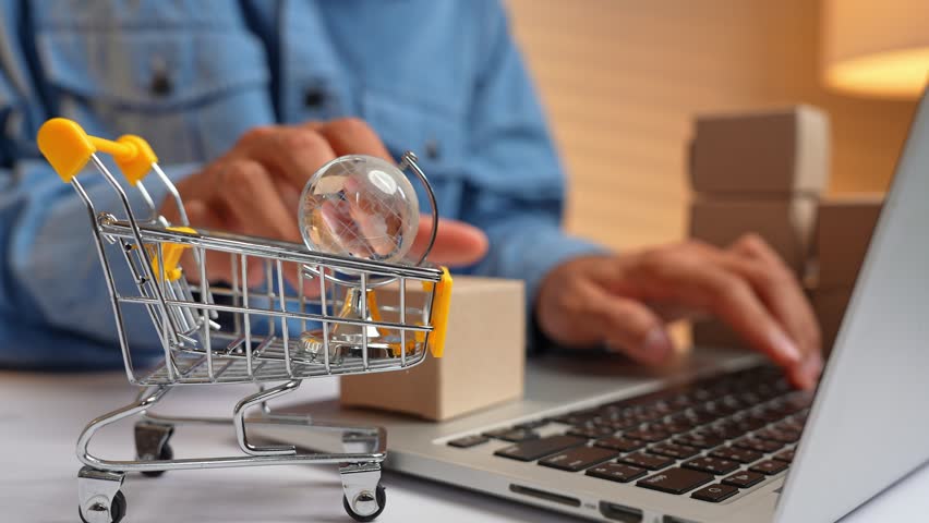 Placing e-commerce boxes in a shopping cart while using a laptop symbolizes online shopping, digital transactions, global commerce, consumer convenience, and the rise of e-commerce logistics.
