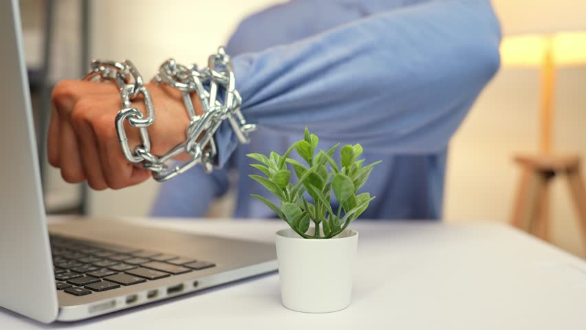 A person with a chained fist raised toward a laptop reflects the frustration, rebellion, or anger from feeling trapped by technology, stress, digital overload, burnout, and the urge to break free.
