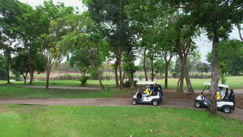 Drone view of group of golfers riding together in golf cart on course. Sporty people and caddy enjoy outdoor recreation lifestyle, and light exercise while driving through lush greenery of the course.