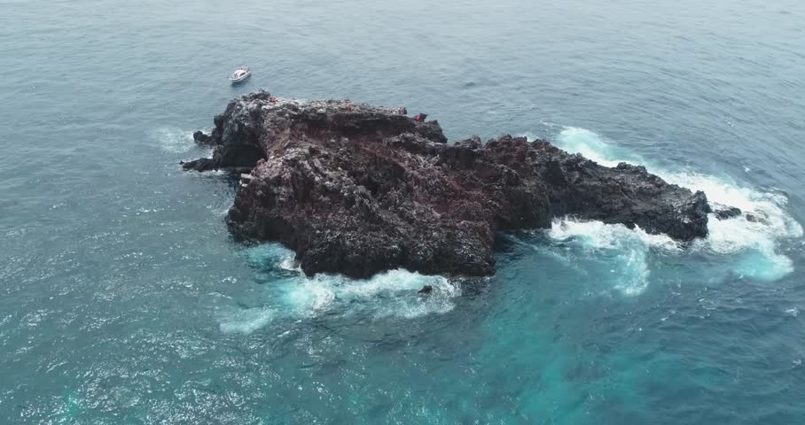 Drone orbit around a small island in the ocean with crashing white waves