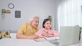 Asian young girl student learning in online class with senior grandma. Adorable little schoolgirl and caring elderly grandmother use digital laptop study remotely with virtual tutor in living room. - Powered by Shutterstock - Get 15% off with code: PIKWIZARD15