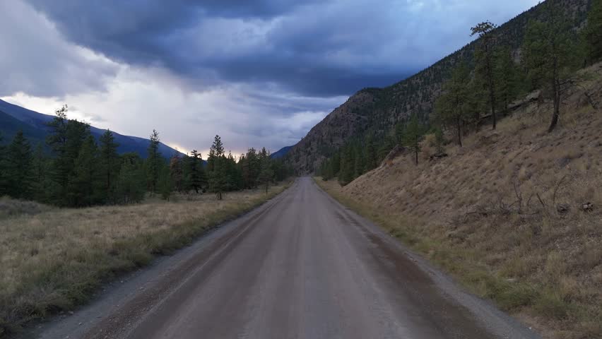 Expansive Dirt Road Cutting Through Wild Landscape of British Columbia Mountains Under Darkening Clouds