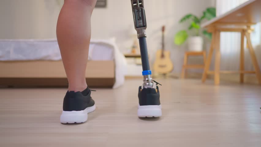Asian man with prosthetic leg relaxing on bed in cozy bedroom at home. Attractive young male amputee wearing a leg brace taking a break during recovery, enjoy everyday routines in house.