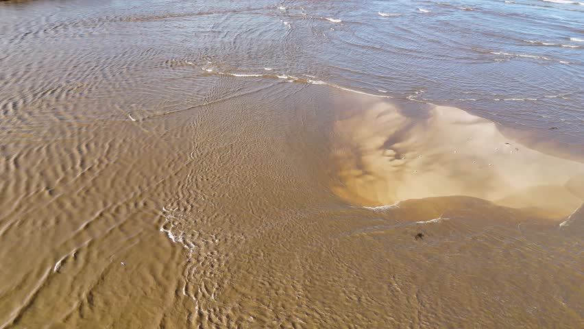 Clear shallow seawater flows over rippled sandbank in sunlight at Nambucca Heads, Australia.