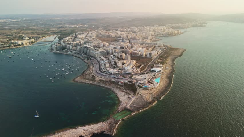 Coastal city at sunset with boats and buildings, aerial view