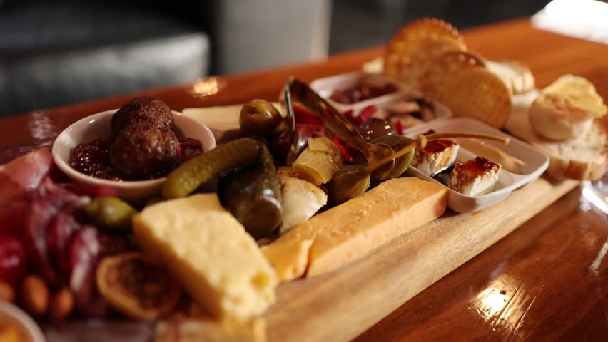 Hand lifts melted cheese from charcuterie board with crackers, pickles, meatballs, and antipasto