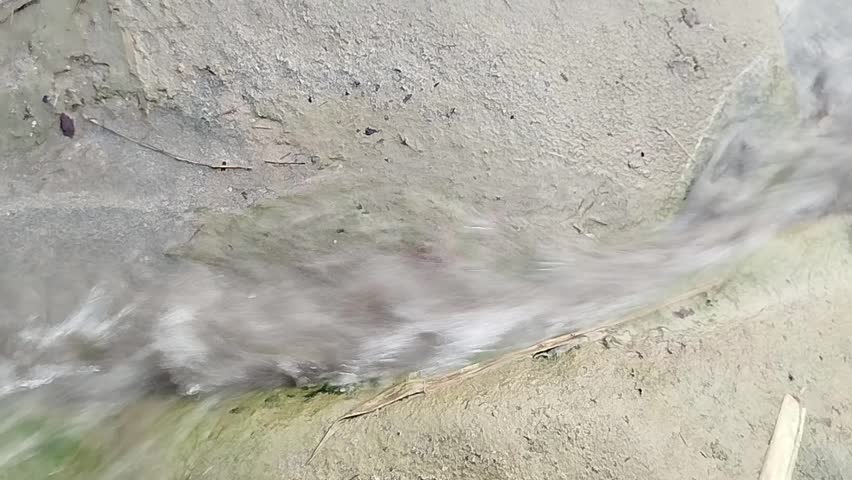 clear water gently trickling through the center of a rustic sack, droplets shimmering in natural light as they weave tiny streams across the textured fabric creating a calm rural moment