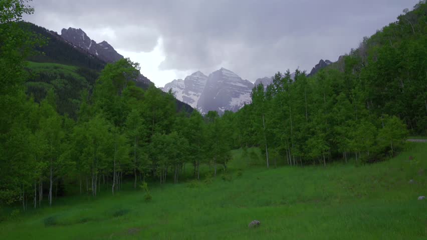 Stormy rainy Maroon Bells Pryamid peaks Wilderness valley Maroon Lake Trailhead rain clouds wet damp lush green basin spring summer landscape Aspen Tree grove White River Forest Maroon Creek zoom in