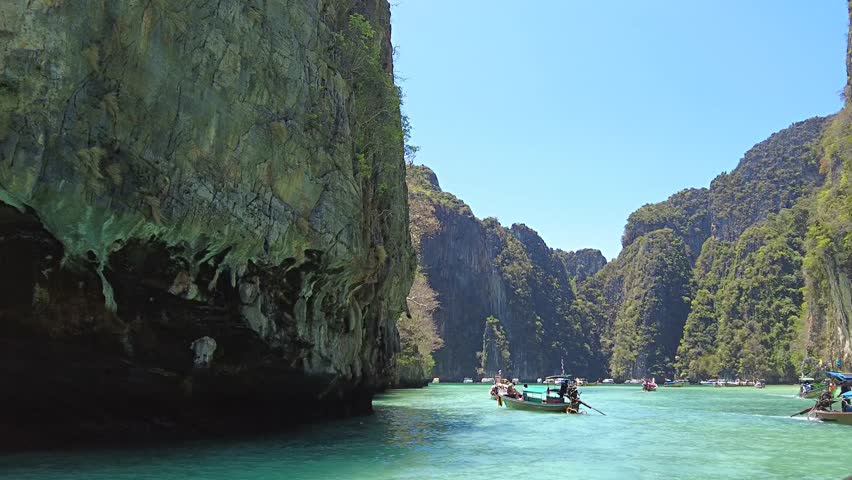 Idyllic boat journey in a serene lagoon flanked by towering cliffs, under the clear blue sky. The turquoise water and lush greenery create a tranquil, picturesque setting.