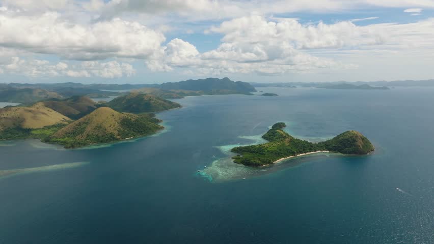 Serene landscape of brown hills in tropical islands surrounded by coral reefs under the clear blue sky and clouds. Coron, Palawan, Philippines.