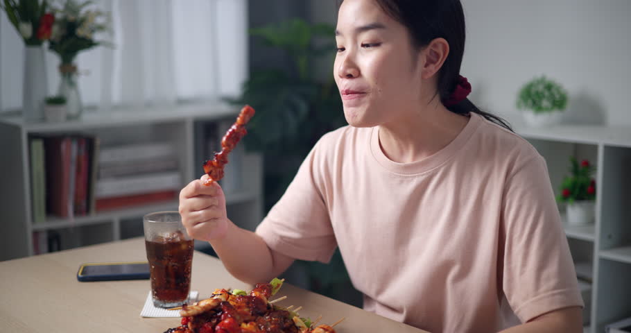 Handheld shot, Smiling Asian woman enjoying delicious barbecue in a cozy dining room. Homemade food. Eating with relaxation