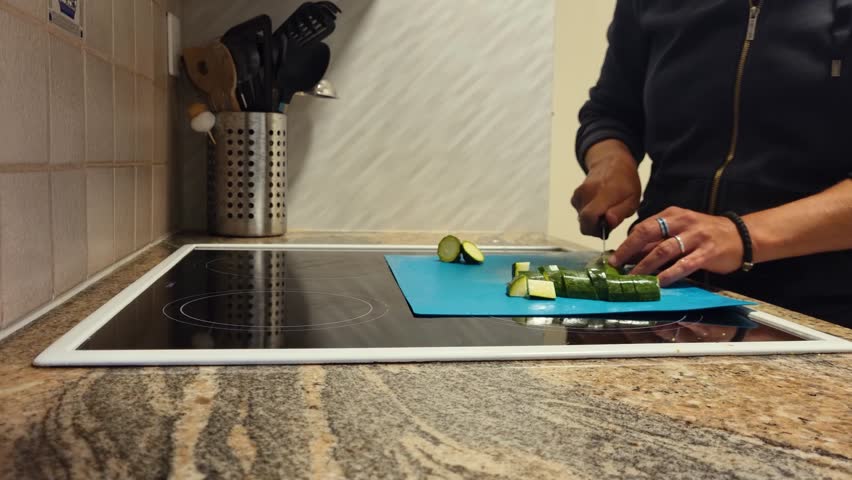 Close-up of a woman’s hands chopping zucchini into small pieces in her home kitchen in Bern, Switzerland, preparing fresh vegetables for a healthy meal