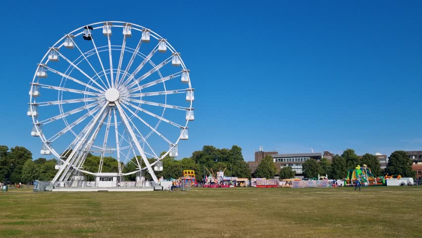 White City View Wheel slowly turns on Parker’s Piece in Cambridge, UK, under a bright blue sky, with the surrounding park and cityscape in view