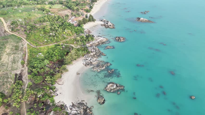 Drone aerial view of a long sandy beach, turquoise clear water, and scattered granite rocks along the tropical coastline. A stunning exotic seashore landscape, perfect for travel and nature themes.