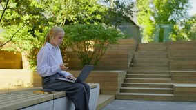 Young woman sits outside with a laptop, wearing wireless earphones, attentively participating in an online video call or virtual class. - Powered by Shutterstock - Get 15% off with code: PIKWIZARD15