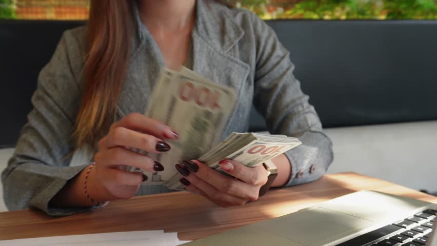 A woman holds several hundred-dollar bills and counts them.
