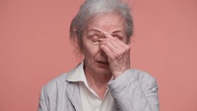 Senior woman in striped jacket holds her forehead and closes her eyes, showing pain and discomfort from a headache, isolated on pink background. - Powered by Shutterstock - Get 15% off with code: PIKWIZARD15