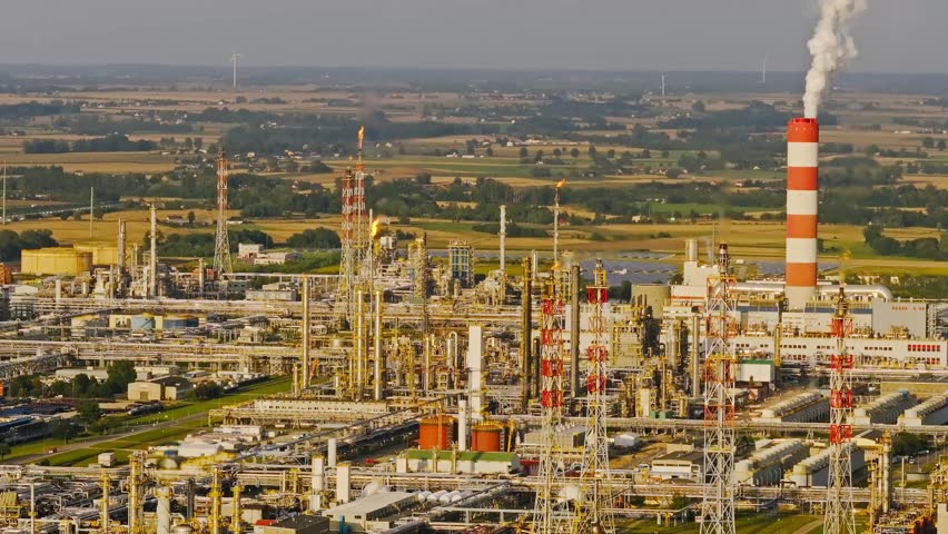Industrial refinery, striped smokestack releasing smoke in countryside fields