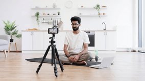 Caucasian adult man in casual outfit recording sports-related vlog discussing smart fitness devices. Room setting is a modern kitchen with exercise equipment visible. - Powered by Shutterstock - Get 15% off with code: PIKWIZARD15