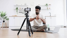 Caucasian adult man in casual outfit recording sports-related vlog discussing smart fitness devices. Room setting is a modern kitchen with exercise equipment visible. - Powered by Shutterstock - Get 15% off with code: PIKWIZARD15