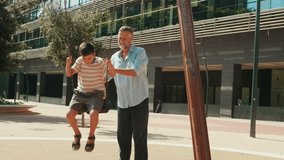 Grandfather pushes grandson on swing set in urban park. Child smiles and laughs having fun bonding with grandpa outdoors. - Powered by Shutterstock - Get 15% off with code: PIKWIZARD15