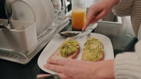 Close up of a woman spreading avocado on toast in the kitchen. She is making a healthy breakfast at home. - Powered by Shutterstock - Get 15% off with code: PIKWIZARD15