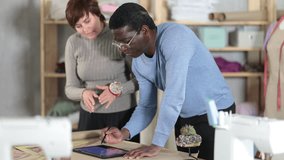 Two interested fashion designers, man and woman, collaborating in sewing studio, using tablet to create and refine new garment design at pattern table, discussing digital sketches or client references - Powered by Shutterstock - Get 15% off with code: PIKWIZARD15