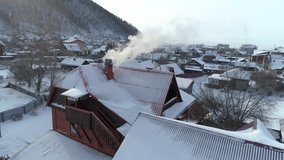 Aerial orbit shot around an old wooden house roof in winter. Smoke rising from chimney, heating with stove, Siberia Russia, Lake Baikal region, cold climate, winter tourism, travel accommodation. 4k - Powered by Shutterstock - Get 15% off with code: PIKWIZARD15