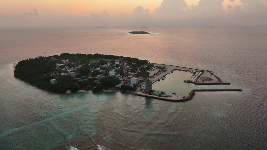 Aerial view of the island of Kamadhoo, featuring a harbor with boats, buildings and lush greenery, bathed in the soft hues of twilight, Kamadhoo, Baa Atoll, Maldives.