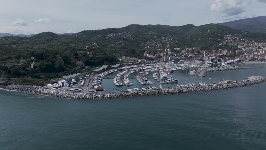 4K Ultra HD drone panoramic footage of a Ligurian marina filled with yachts and boats, surrounded by breakwaters, hills, and coastal town.