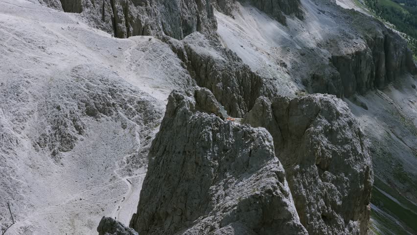 Aerial flying backwards to reveal Rifugio Passo Santner, a remote mountain refuge perched on rocky cliffs of Dolomites, Italy
