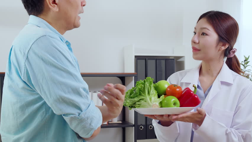 Asian nutritionist holding fresh fruits vegetables during consultation with patient in clinic, wellness and healthy eating, woman dietitian or consultation explaining nutrition for weight loss advice.