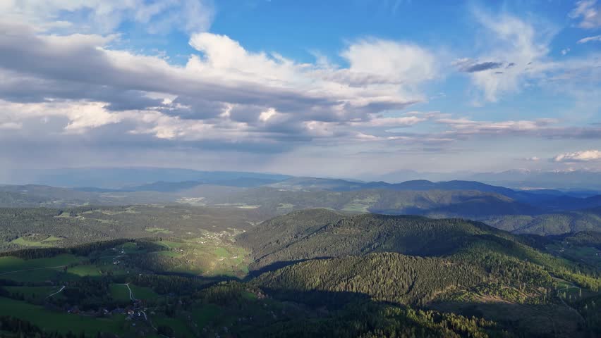 Aerial view of lush green forest and mountain landscape under a partly cloudy sky creating a scenic view from above, Hochrindl, Kärnten, Austria.